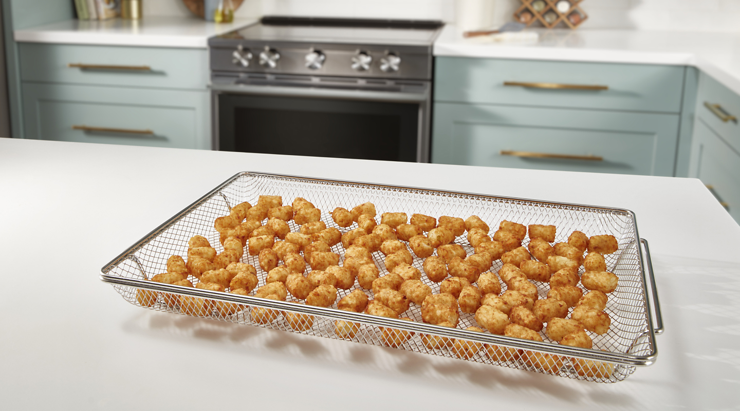 An air fry basket with tater tots sitting on a white countertop.