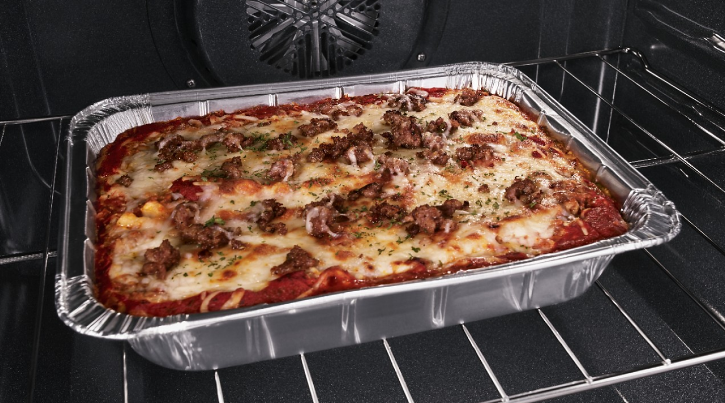 Lasagna in aluminum foil pan on oven rack.