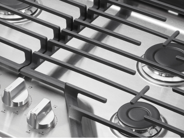 Closeup of stainless steel cooktop knobs, burners, and grates