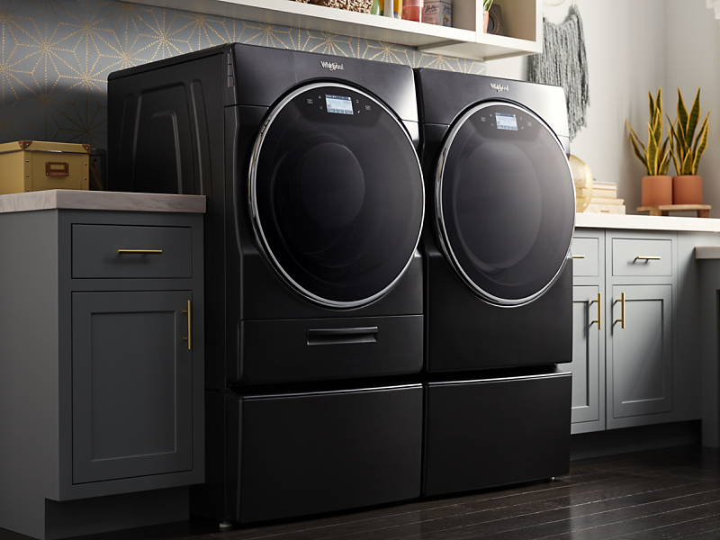 Whirlpool® Front Load Washer and Dryer in Black Shadow in a laundry room with gray cabinets