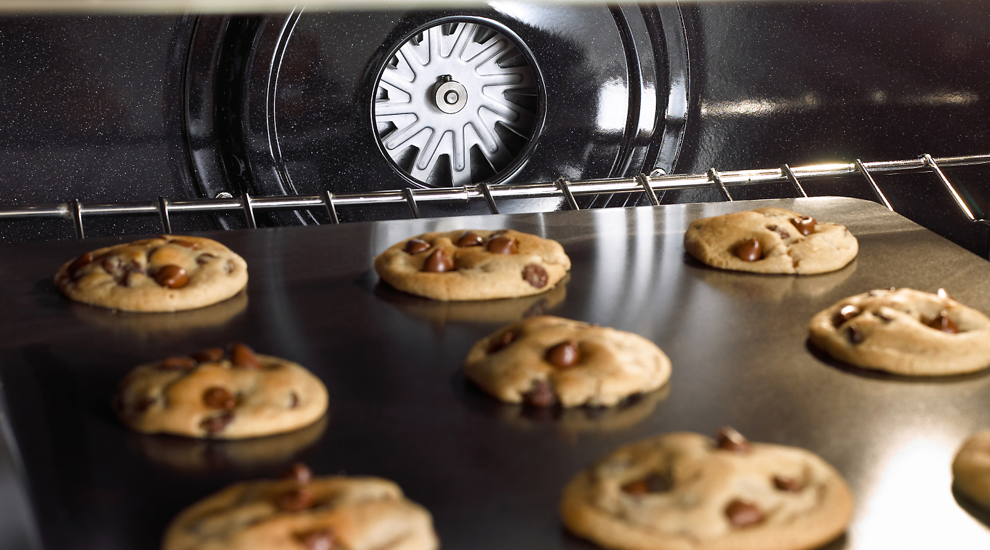 A sheet of chocolate chip cookies baking in an oven.