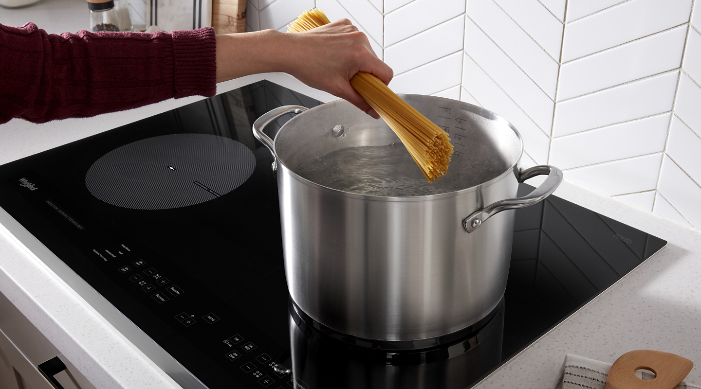 Hand adding pasta to boiling water on cooktop