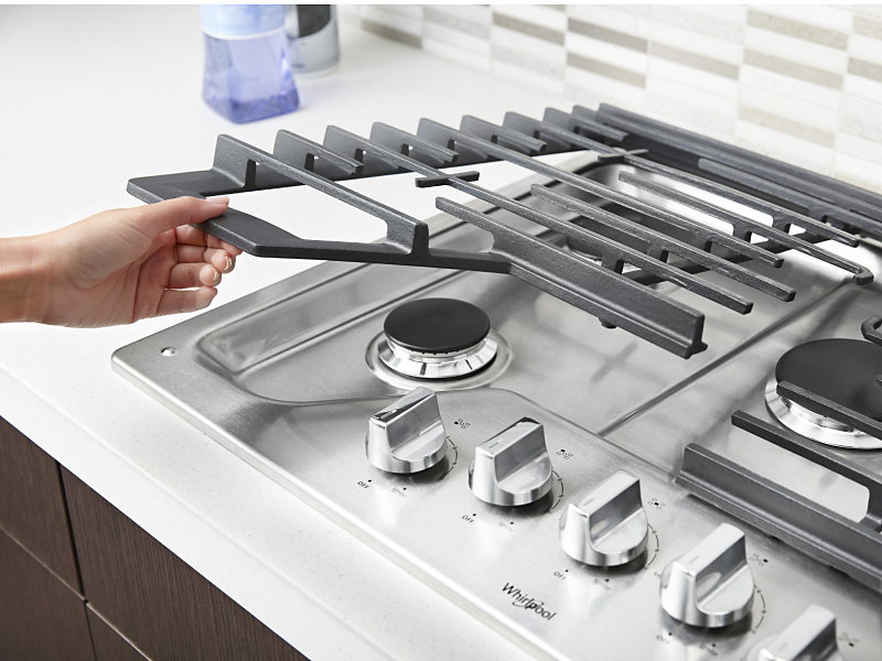 Hand lifting metal grates off of gas cooktop
