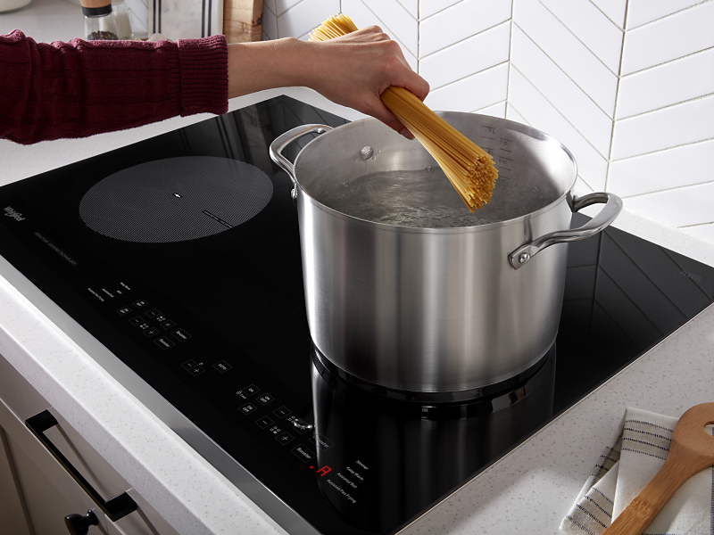 Hand adding pasta to boiling water on cooktop