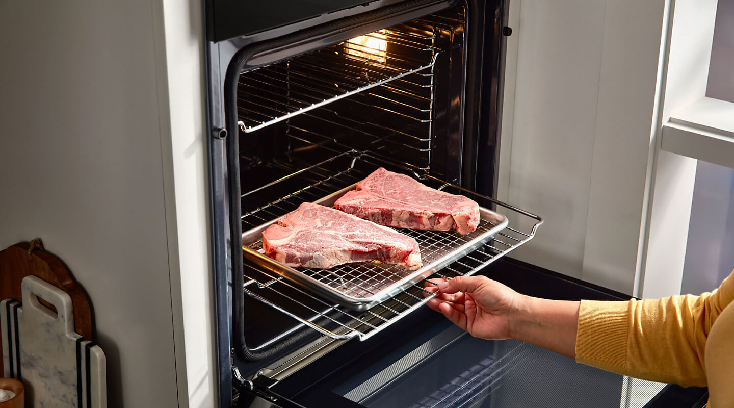 Person putting two steaks in a Whirlpool® wall oven