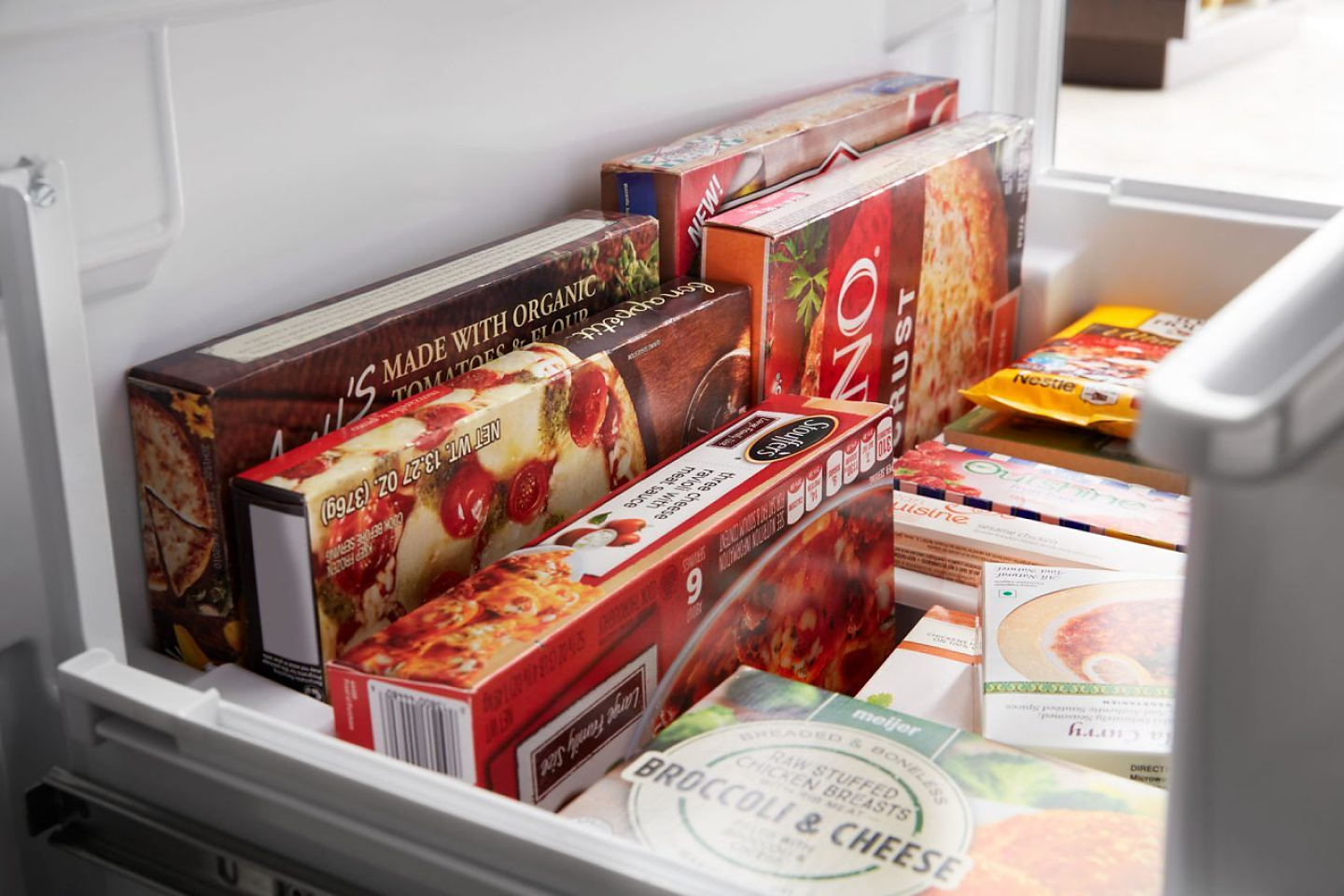 Close-up of frozen pizzas and other foods in an open bottom freezer