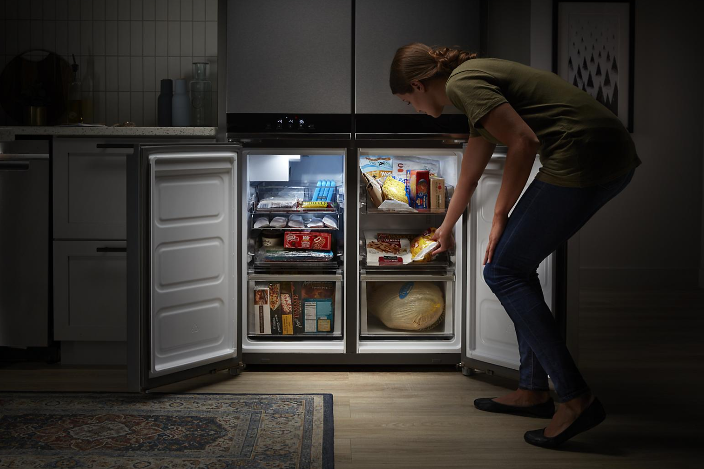  Person putting frozen in food in open doors of a four-door refrigerator freezer