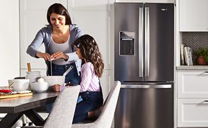 Woman and child cooking on counter in front of a French door refrigerator