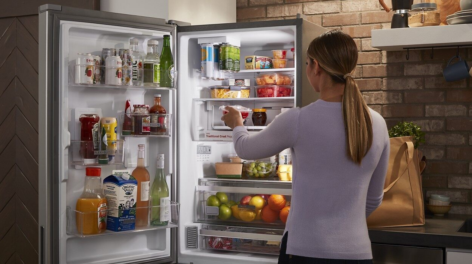 一名妇女打开冰箱门，挑选一盒水果