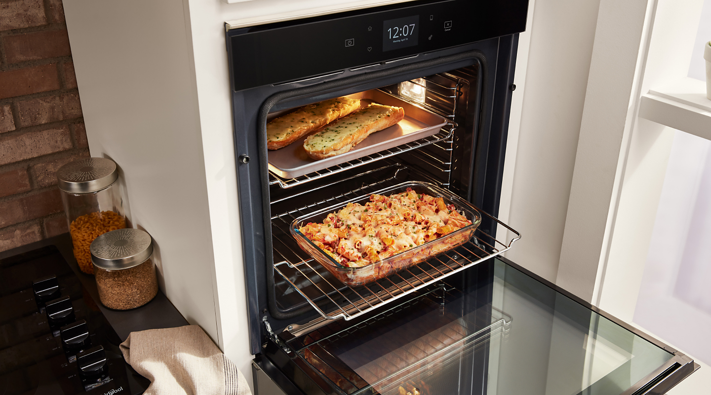 Open wall oven cooking garlic bread on the top rack and pasta on the bottom rack