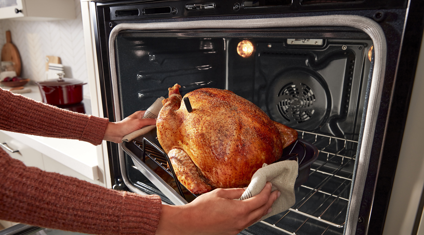 Person using oven mitts to pull a roasted turkey from the oven