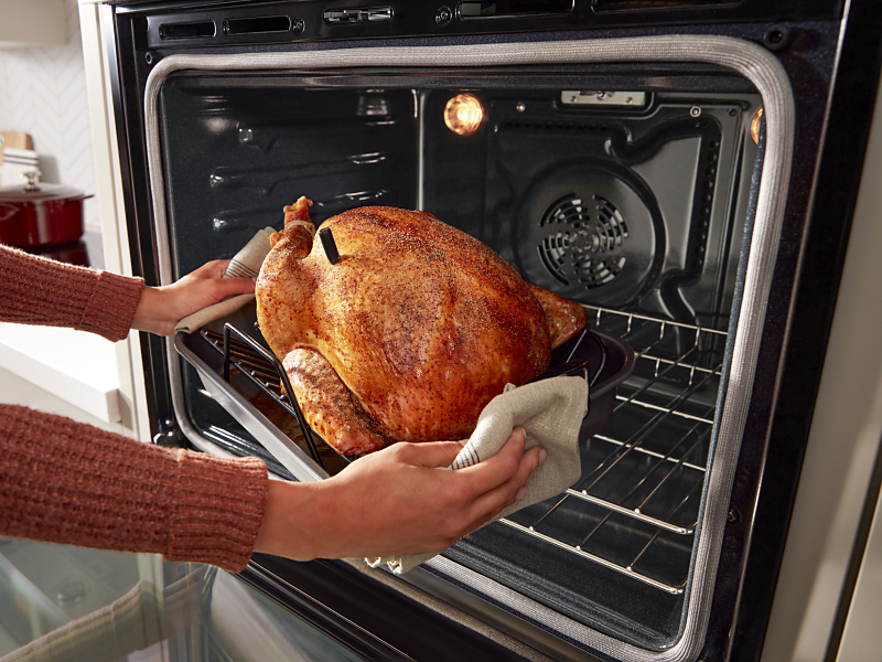 Person using oven mitts to pull a roasted turkey from the oven