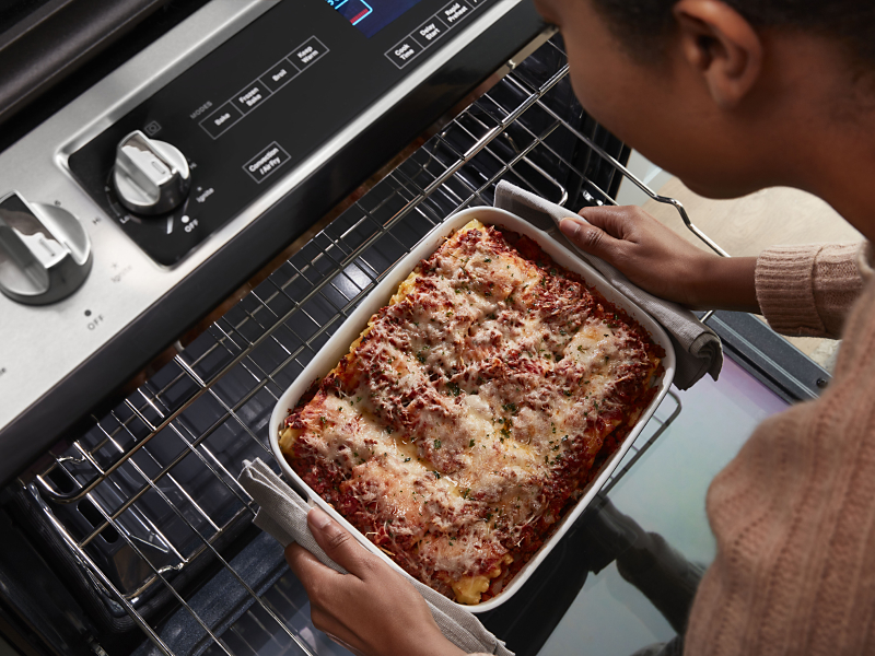Top view of a person pulling casserole out of the top rack of an oven