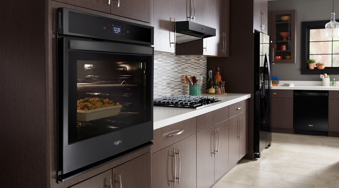 Black Whirlpool® wall oven cooking food in a kitchen featuring a gas range and neutral tile backsplash