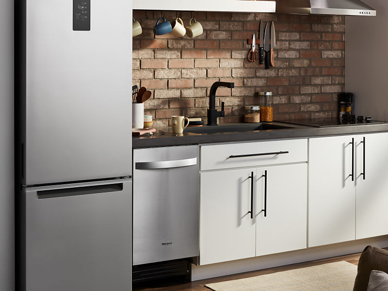 A stainless steel Whirlpool® dishwasher, refrigerator and oven in a modern kitchen.