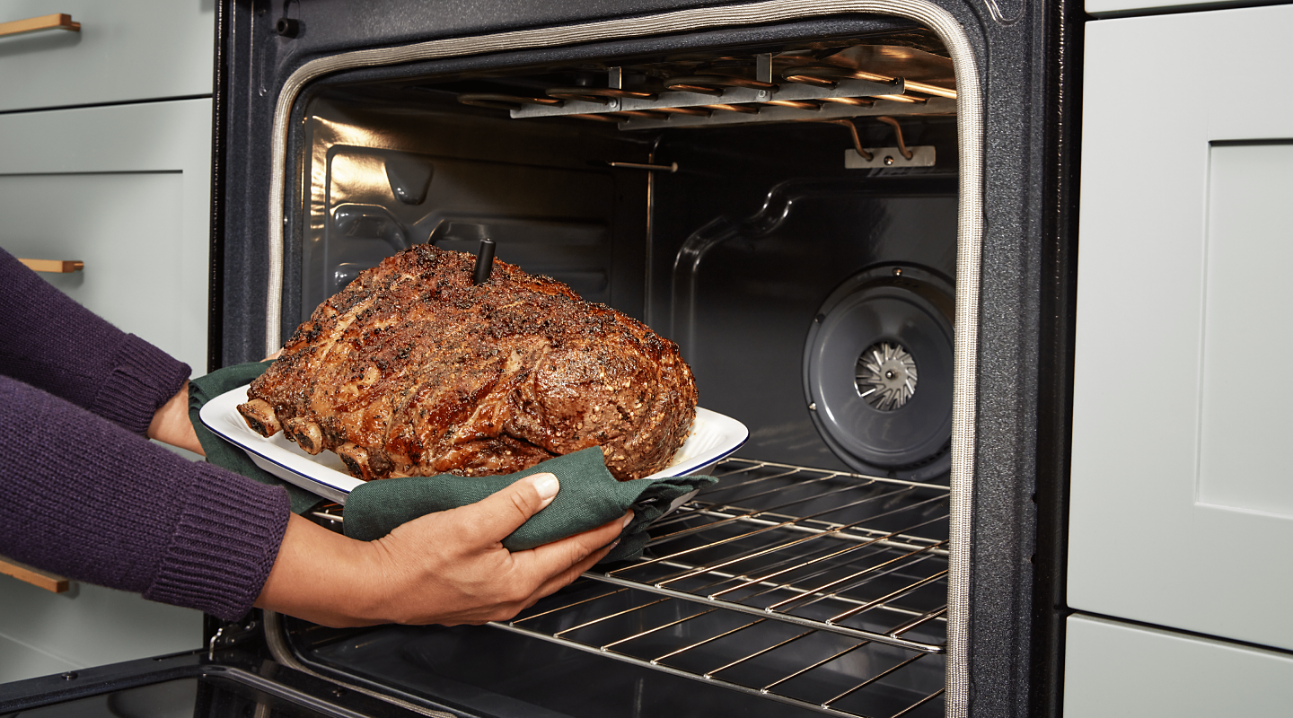 A person removing a roast from the oven.