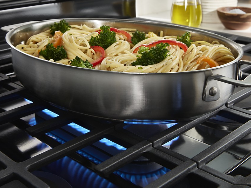 A pasta dish with vegetables cooking on a gas range burner