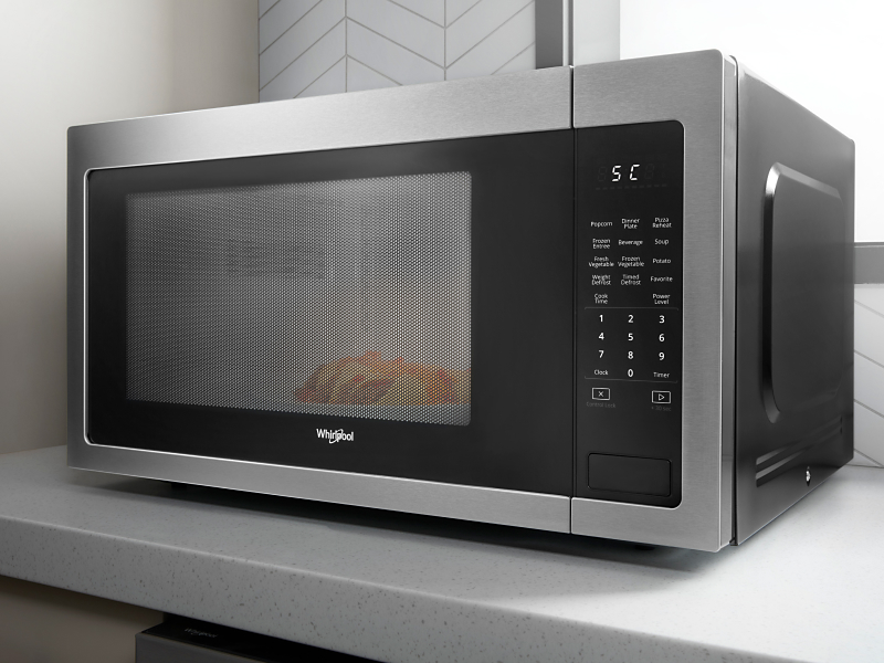 Silver and black countertop microwave from Whirlpool brand cooking food