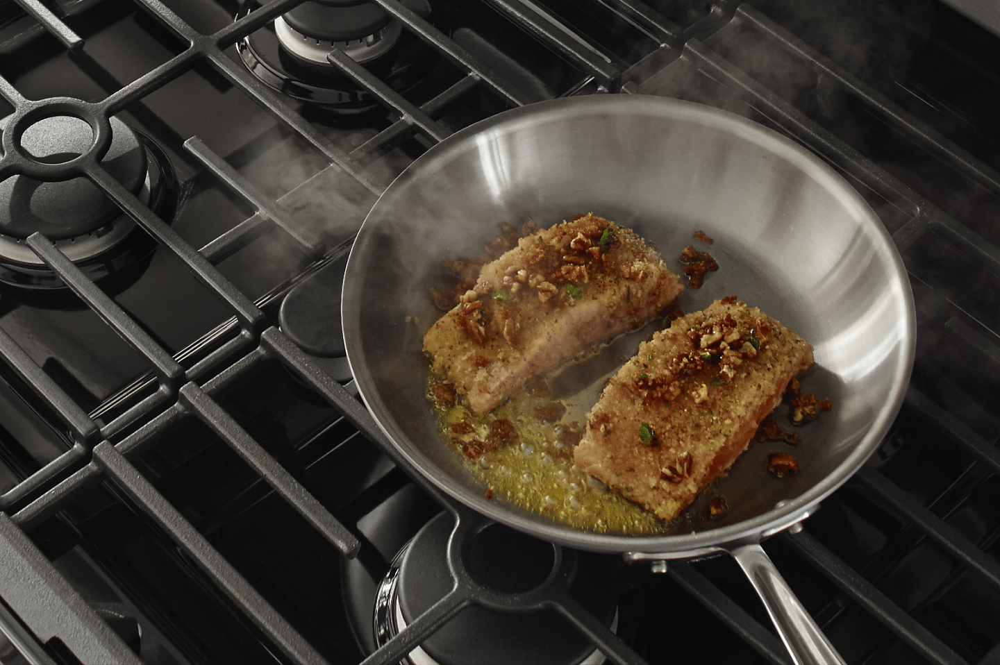 Fish filets simmering in a stainless steel pan with oil