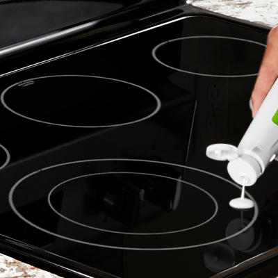 Person dripping white stovetop cleaner on electric cooktop burner