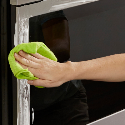 Person wiping oven’s stainless steel perimeter with green rag and cleaner