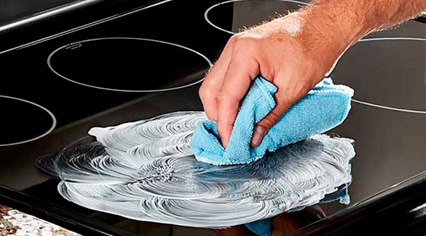 Person using blue towel to apply cleaner to glass electric stovetop burner