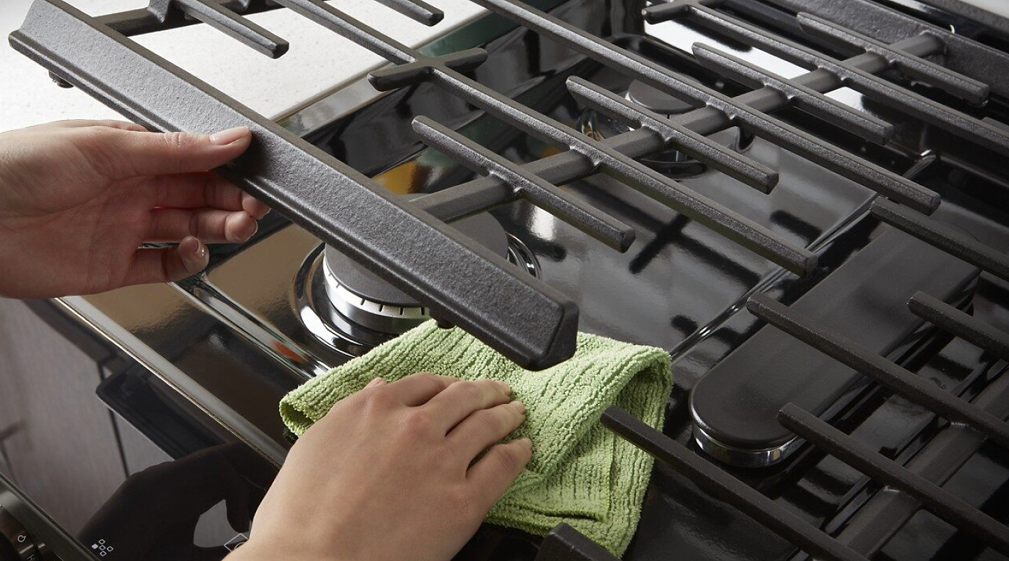 A person lifting up stove grates to clean underneath.