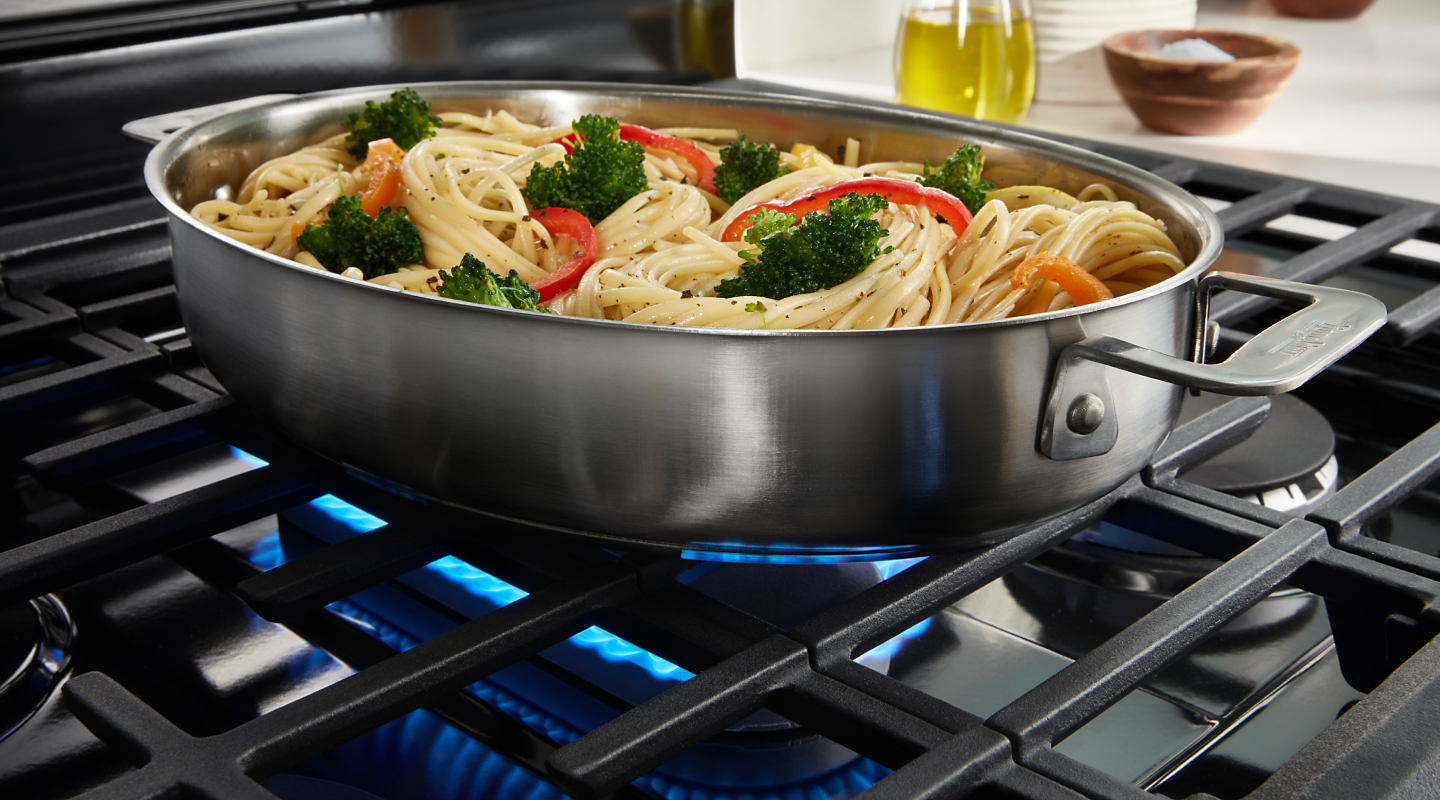 Spaghetti and vegetables cooking on a stovetop.