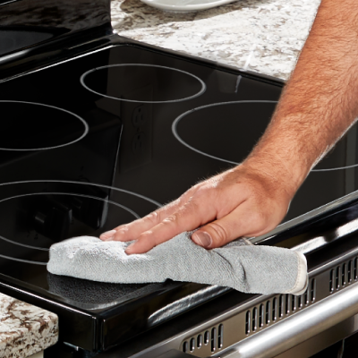 Person wiping a Whirlpool® induction cooktop with a cloth.