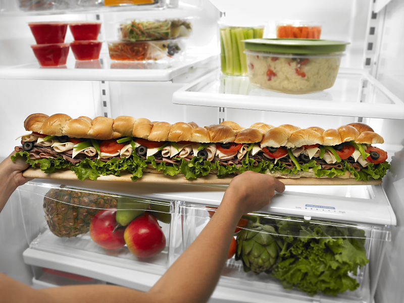 Person placing a party sub sandwich in a refrigerator