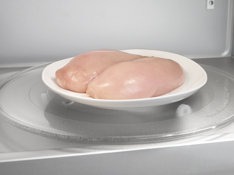Two raw chicken breasts on a microwave-safe plate inside the microwave