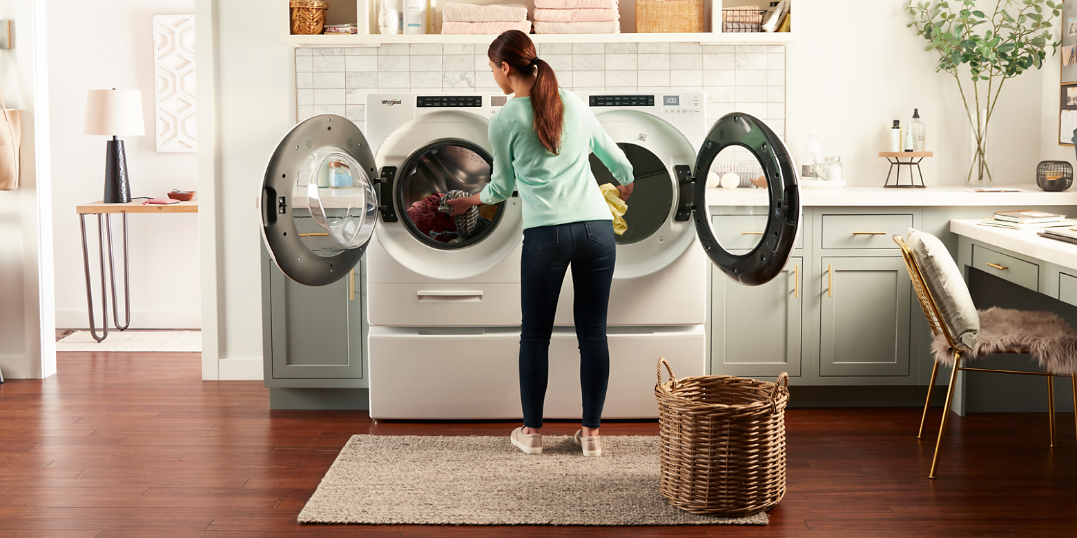 A person doing laundry with a Whirlpool® side-by-side laundry set.