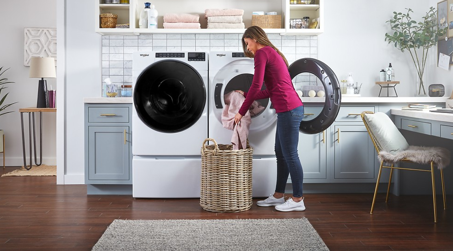 Woman loading sheets into laundry basket from dryer.
