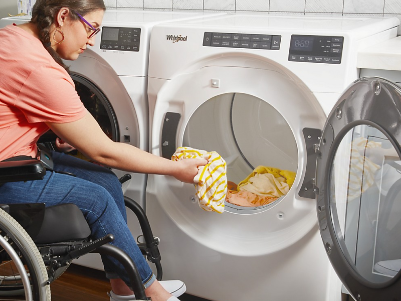 Woman in a wheelchair loading her Whirlpool® dryer with clothing.