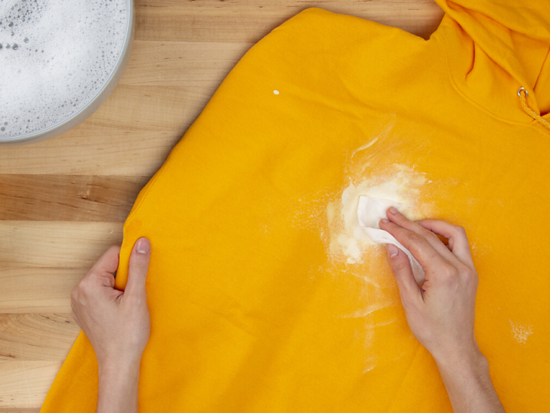 Hand blotting white paint on a yellow sweatshirt with a paper towel