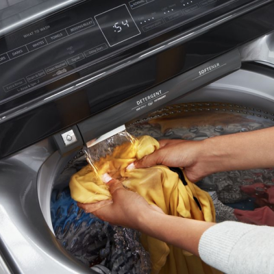 Person rinsing a garment under a built-in water faucet in a Whirlpool® washing machine