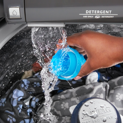 A person rinsing a detergent cap under the running water of a washer