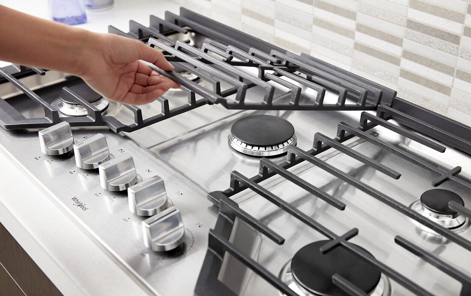 Hand lifting a grate on a gas cooktop