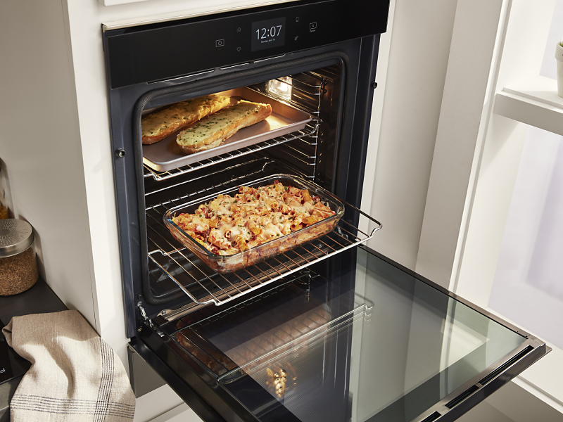 Open Whirlpool®  single wall oven showing a tray of garlic bread and casserole dish