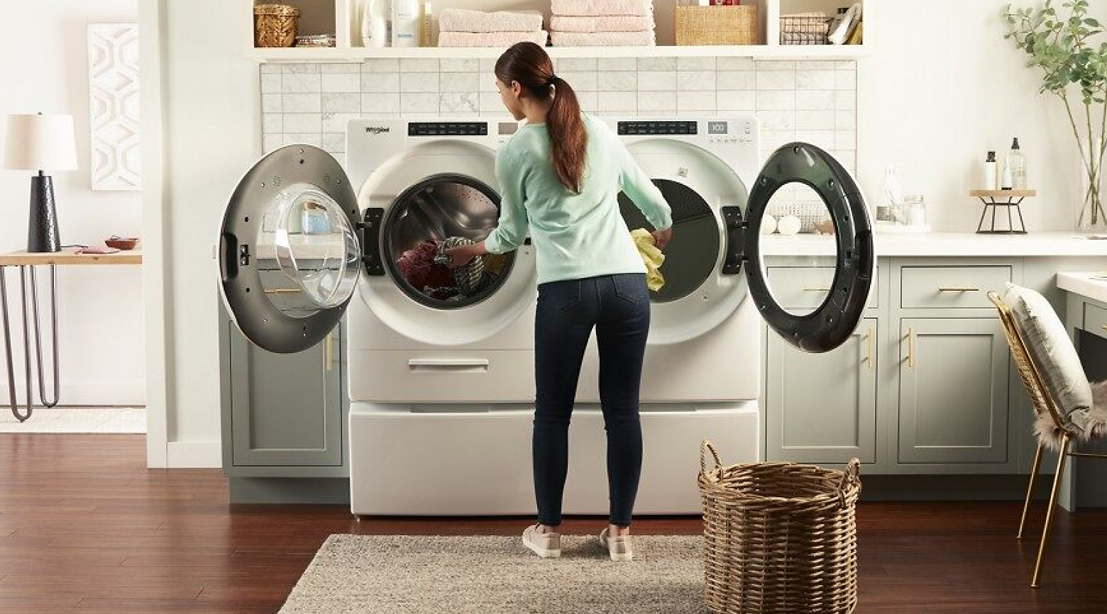 A woman transferring laundry from a front load washer to a front load dryer.