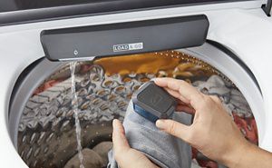 Person scrubbing a garment over a Whirlpool® Top Load Washing Machine with Built-In Faucet.