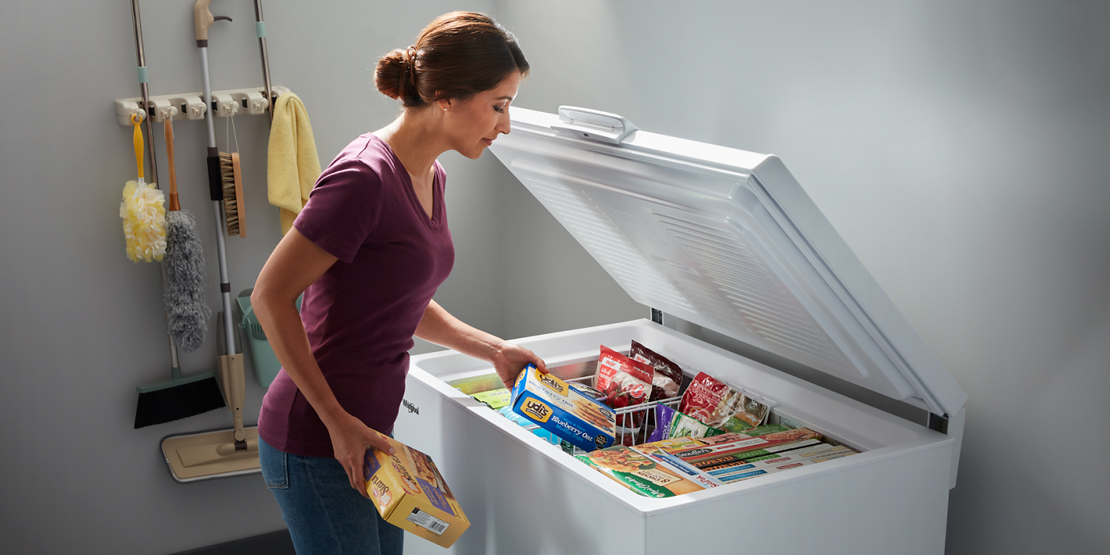 Woman placing food in white chest freezer baskets