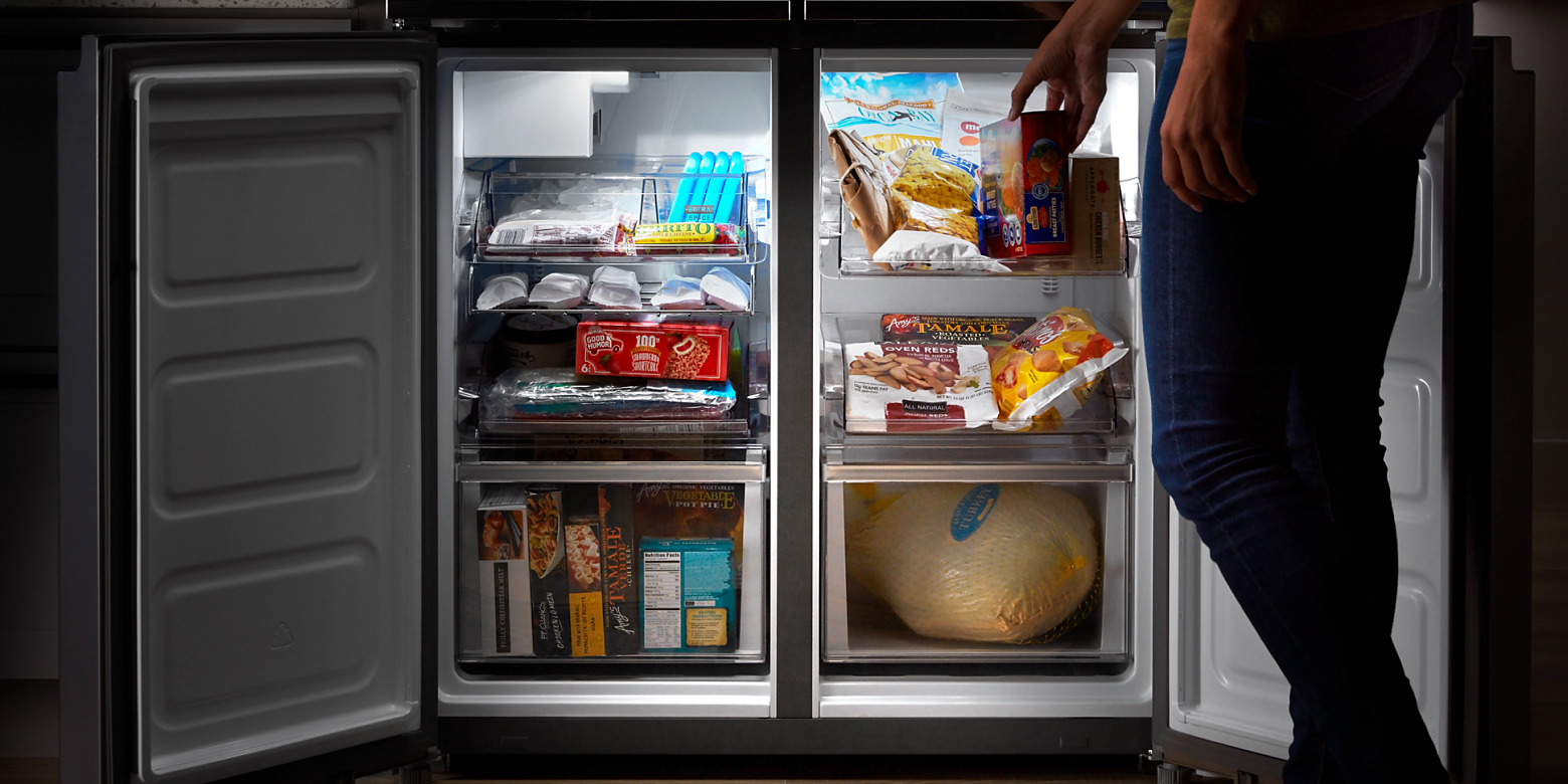 Side-by-side freezer drawers opened with person placing item in freezer