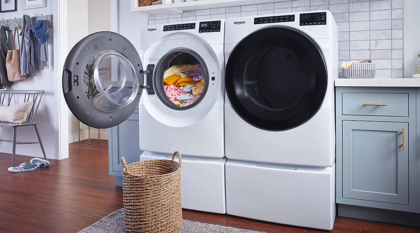 Whirlpool® white washer and dryer pair with the door open next to a laundry basket