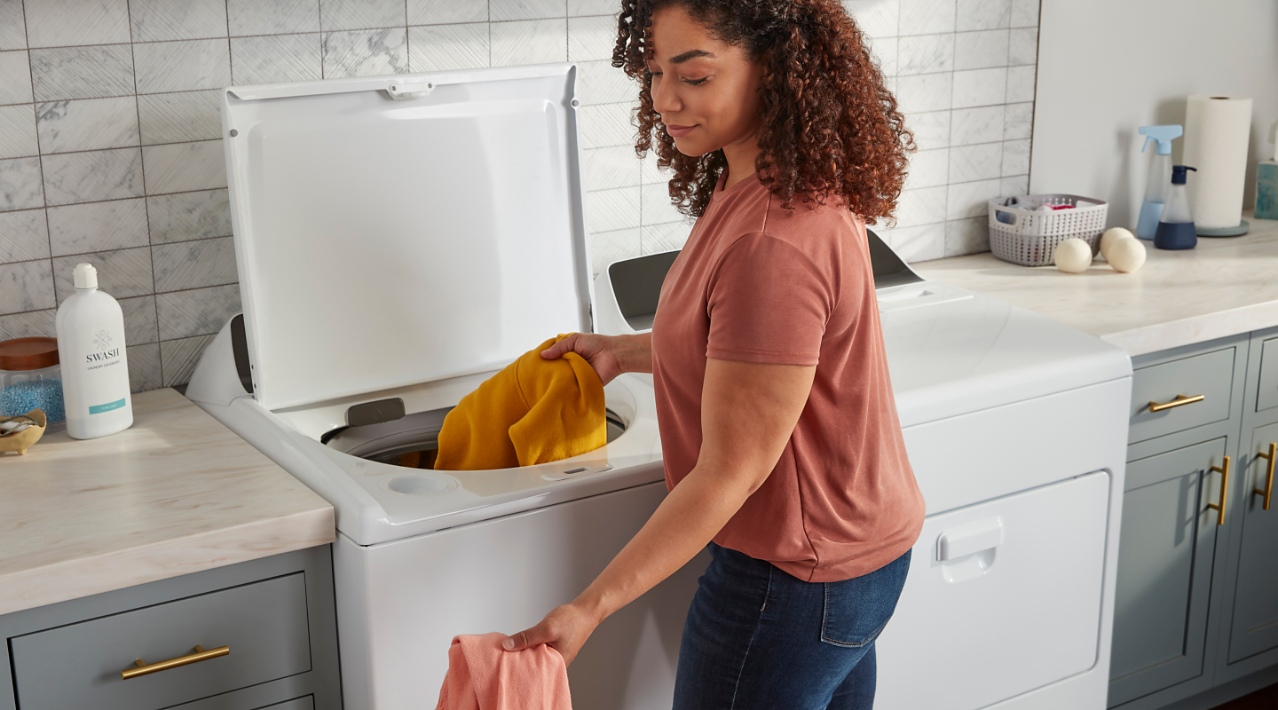 A woman puts clothes into a washer