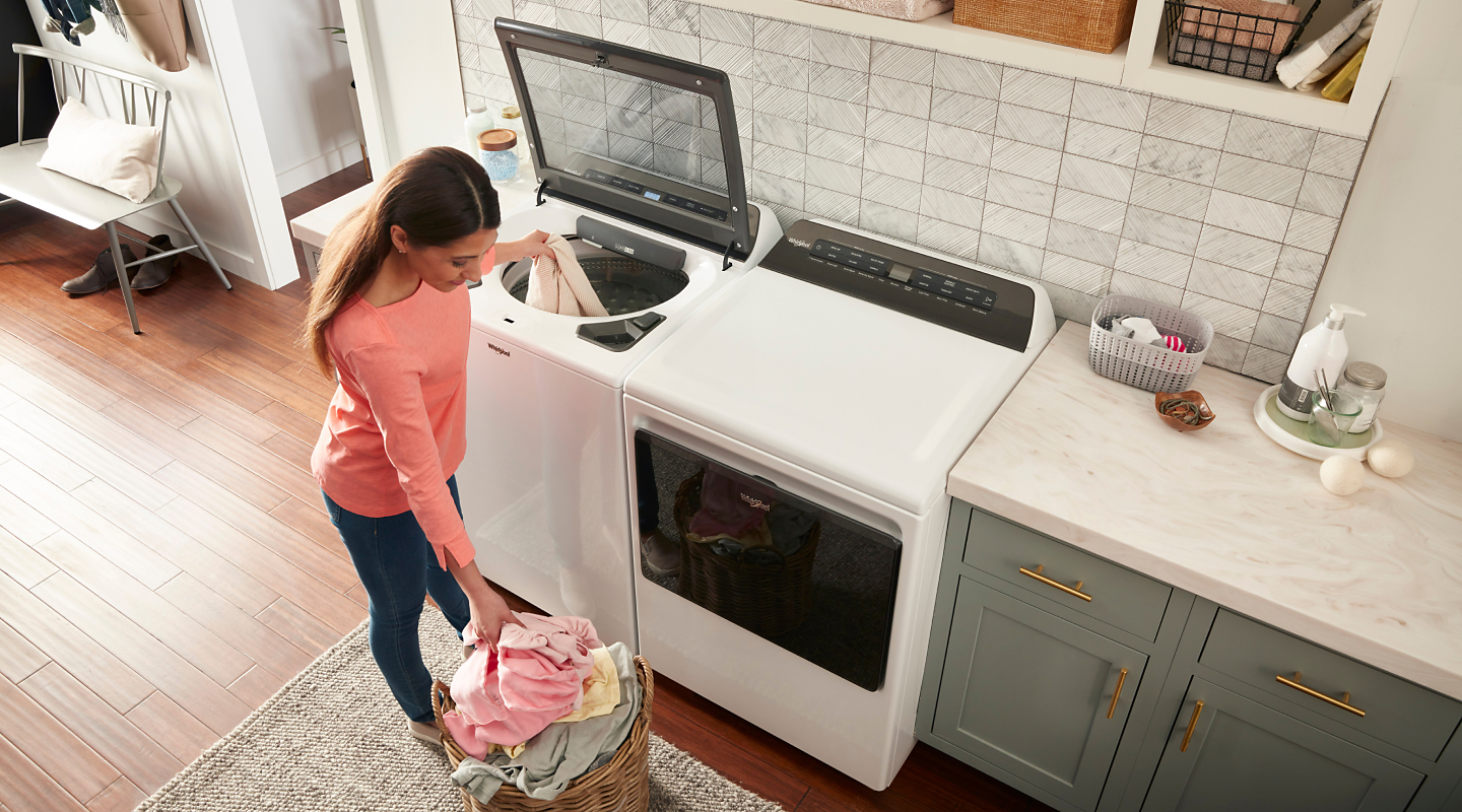 A woman putting a load of laundry into a top load washer