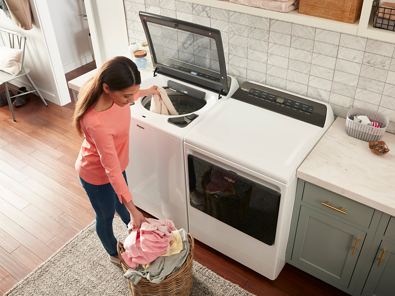 A woman putting a load of laundry into a top load washer