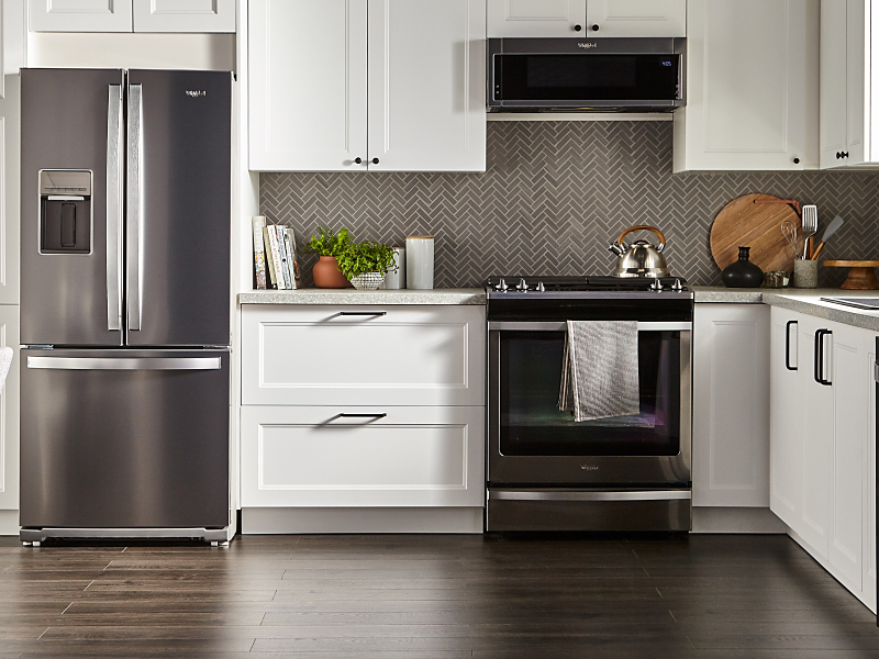 Whirlpool oven and over-the-range microwave in a kitchen with gray herringbone tile backsplash and white cabinets.