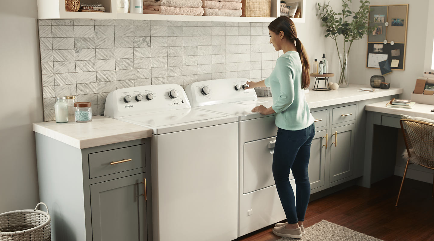 A woman using a Whirlpool® dryer next to a matching washer