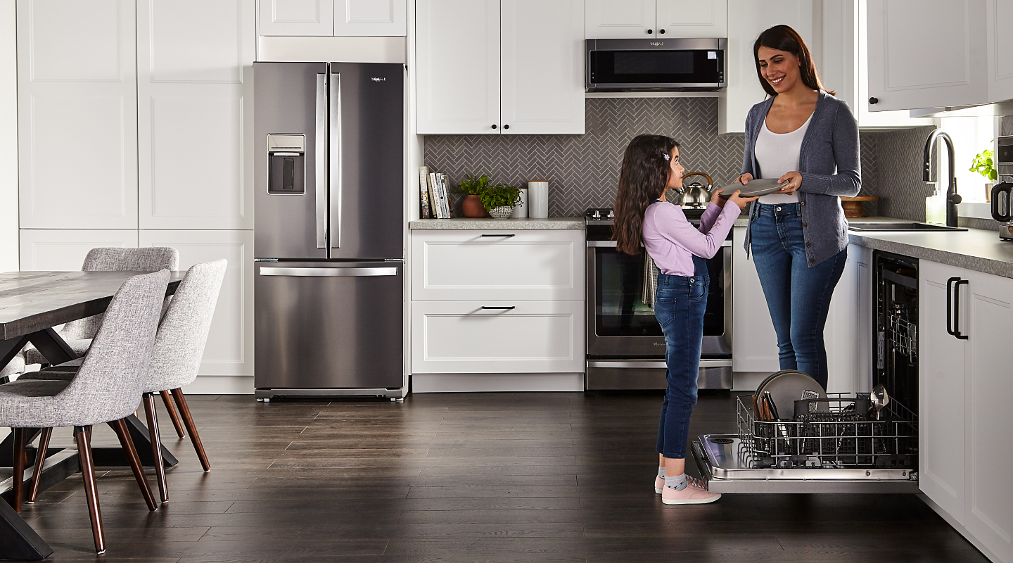 A mother and daughter unloading a Whirlpool® dishwasher.